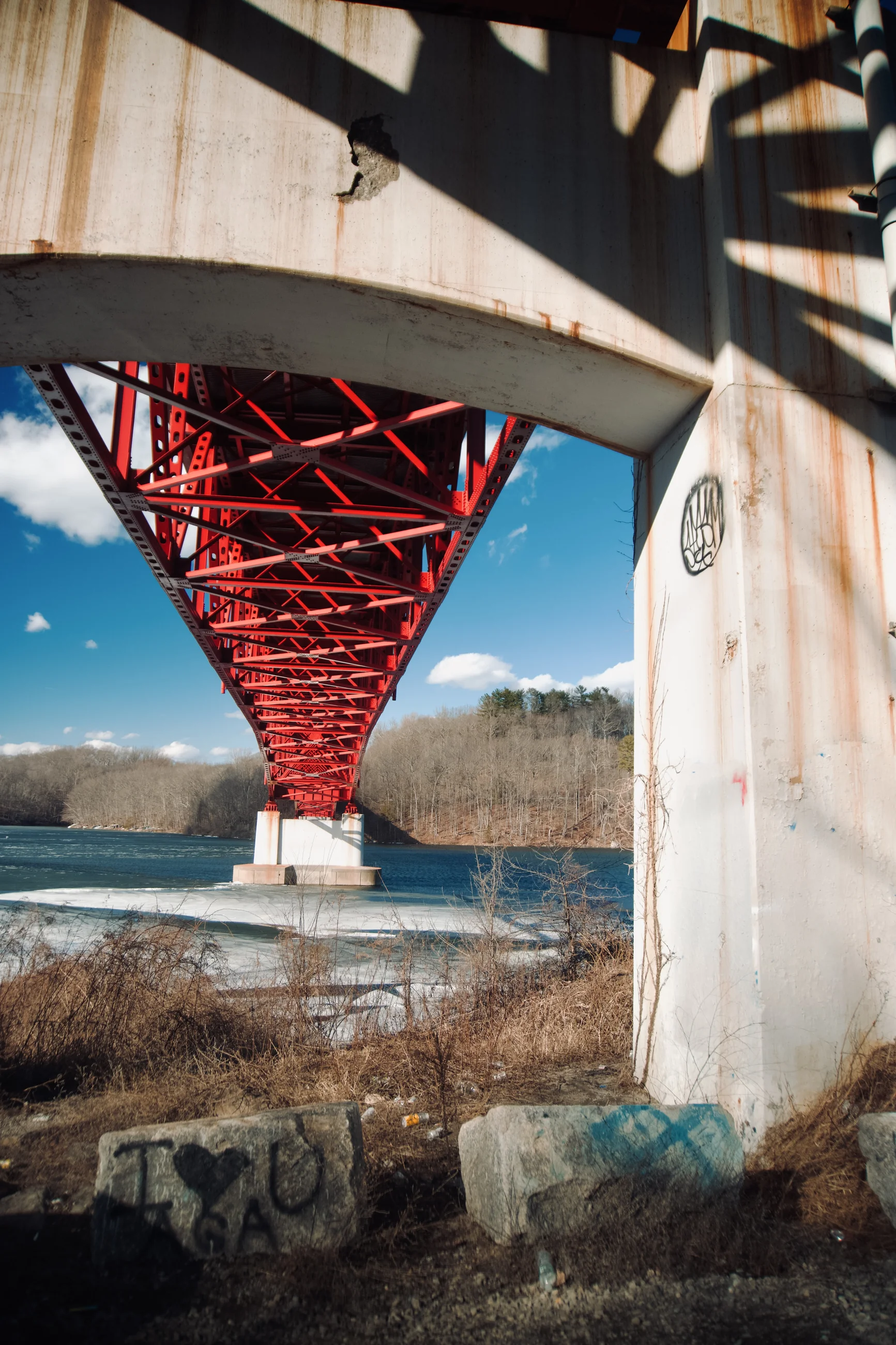 Red bridge structure seen from underneath beside the water